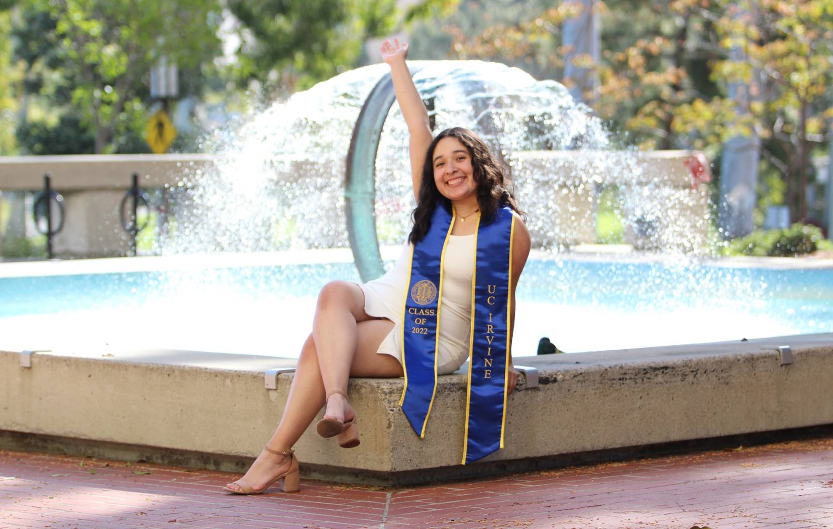 Young woman with UC Irvine stole smiling at a fountain