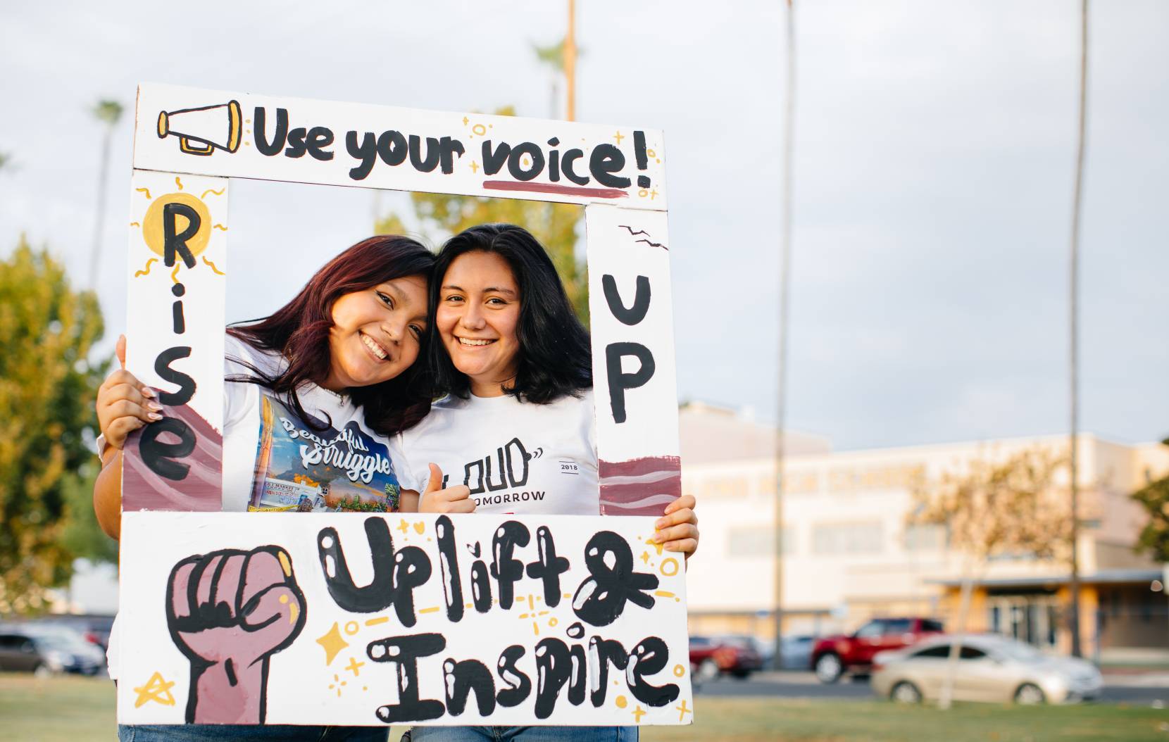 Two young women in an Use Your Voice Uplift and Inspire cardboard frame