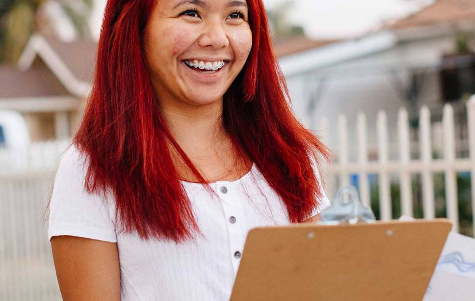 Young woman with dyed red hair holds a clipboard and smiles