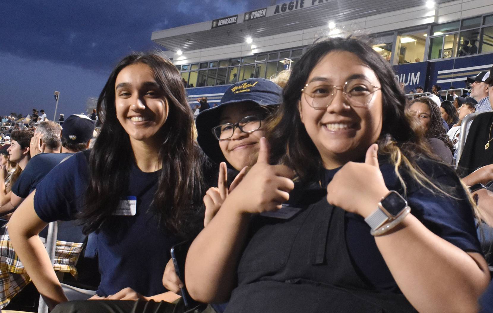Three students pose for a photo at UC Berkeley's stadium at night, giving thumbs up