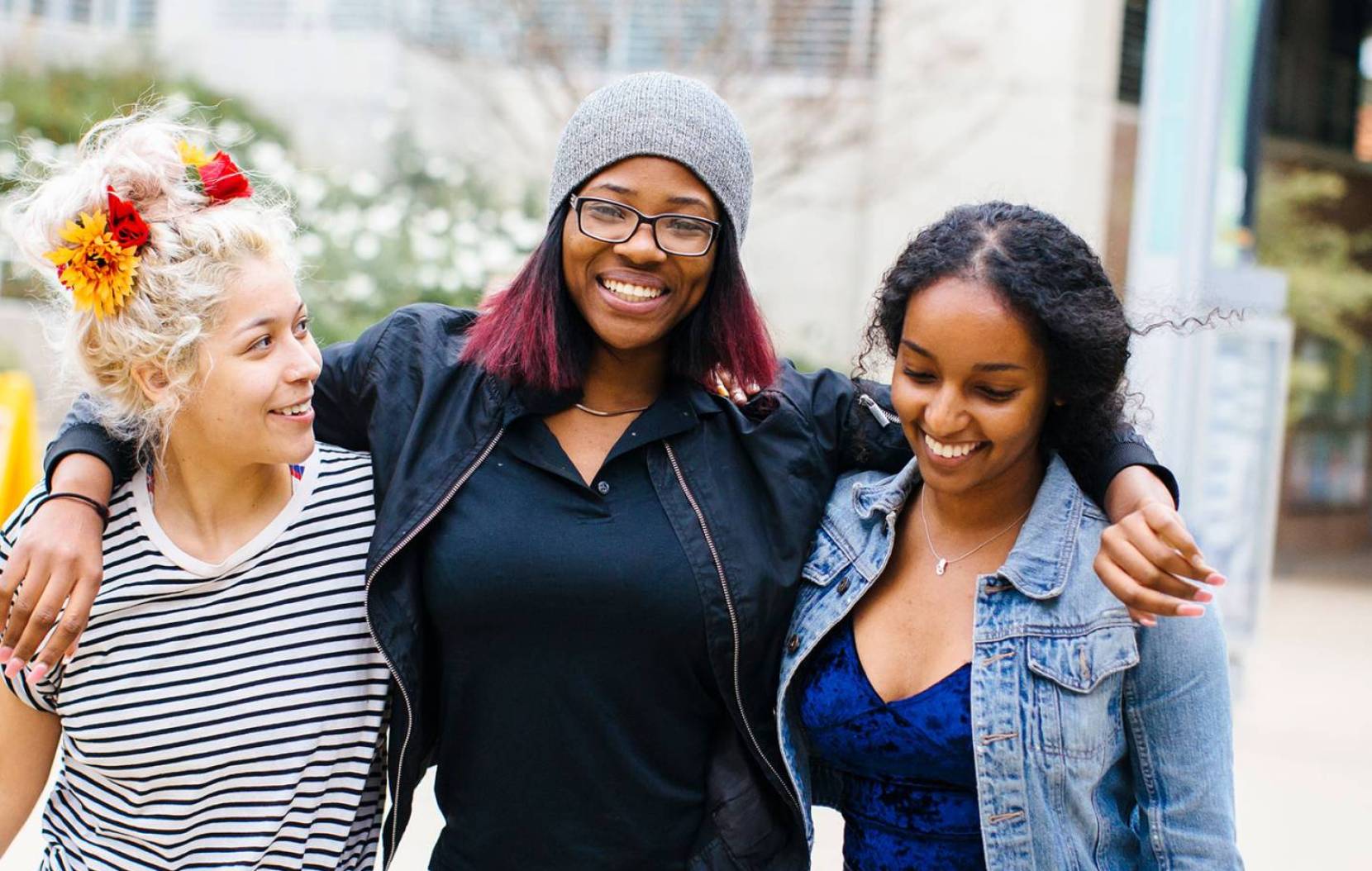 Three students with their arms around each other walking on campus