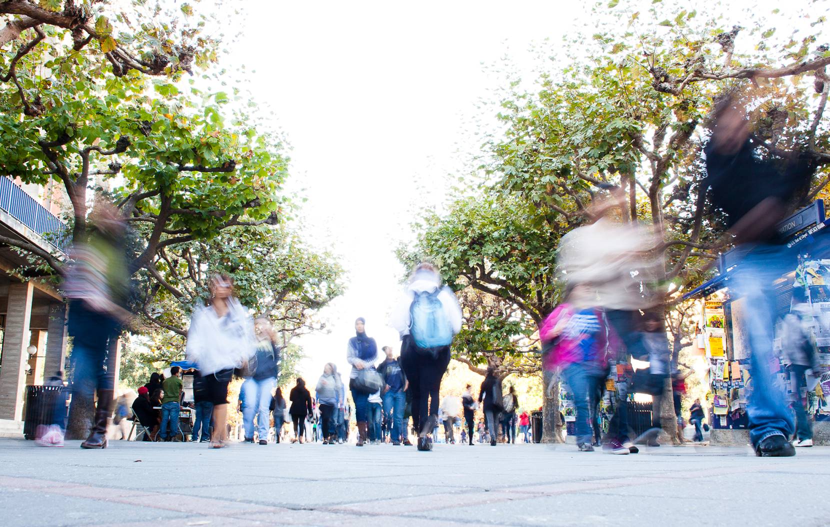 A crowd of blurred students walking across a campus quad