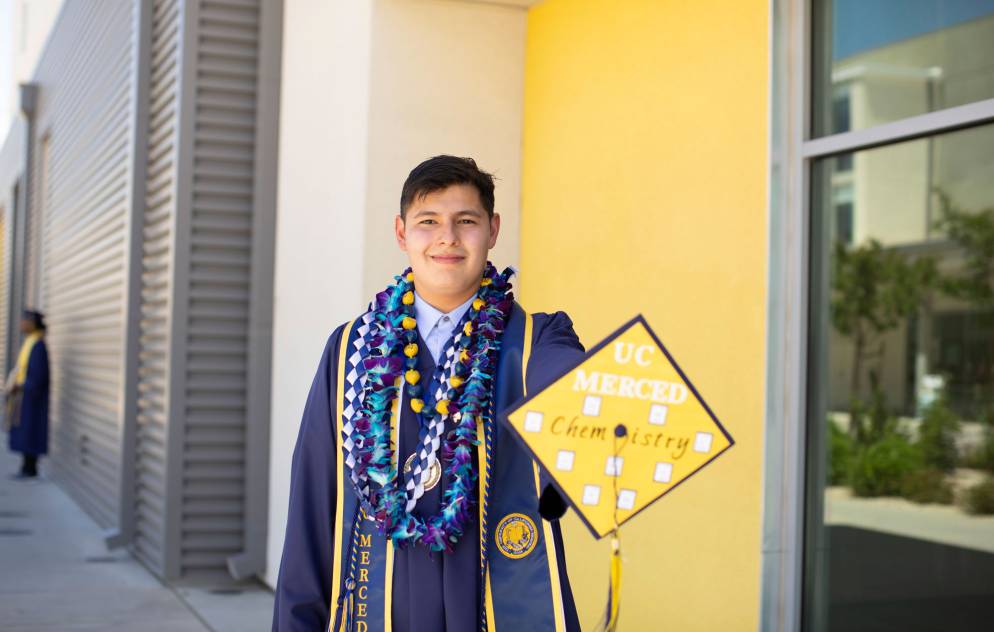 Young Hispanic male in UC Merced graduation stole and gown shows cap with the word chemistry on it