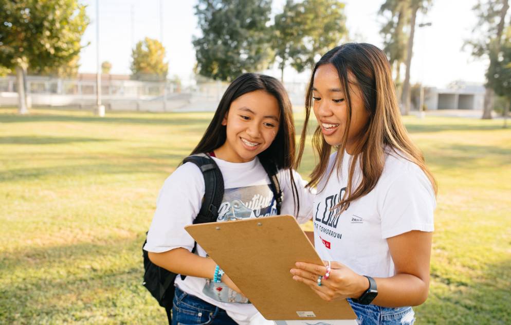 Two students outside looking at a clipboard together.