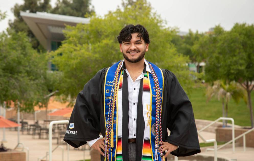 Zabdi Velazquez smiles at the camera wearing colorful garlands around his neck and a graduation gown.