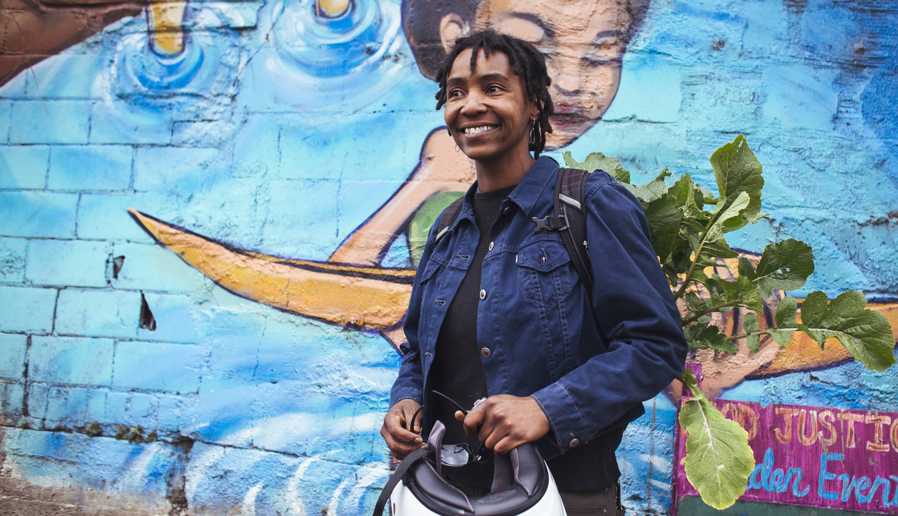 African American woman holding a scooter helmet in front of a colorful mural