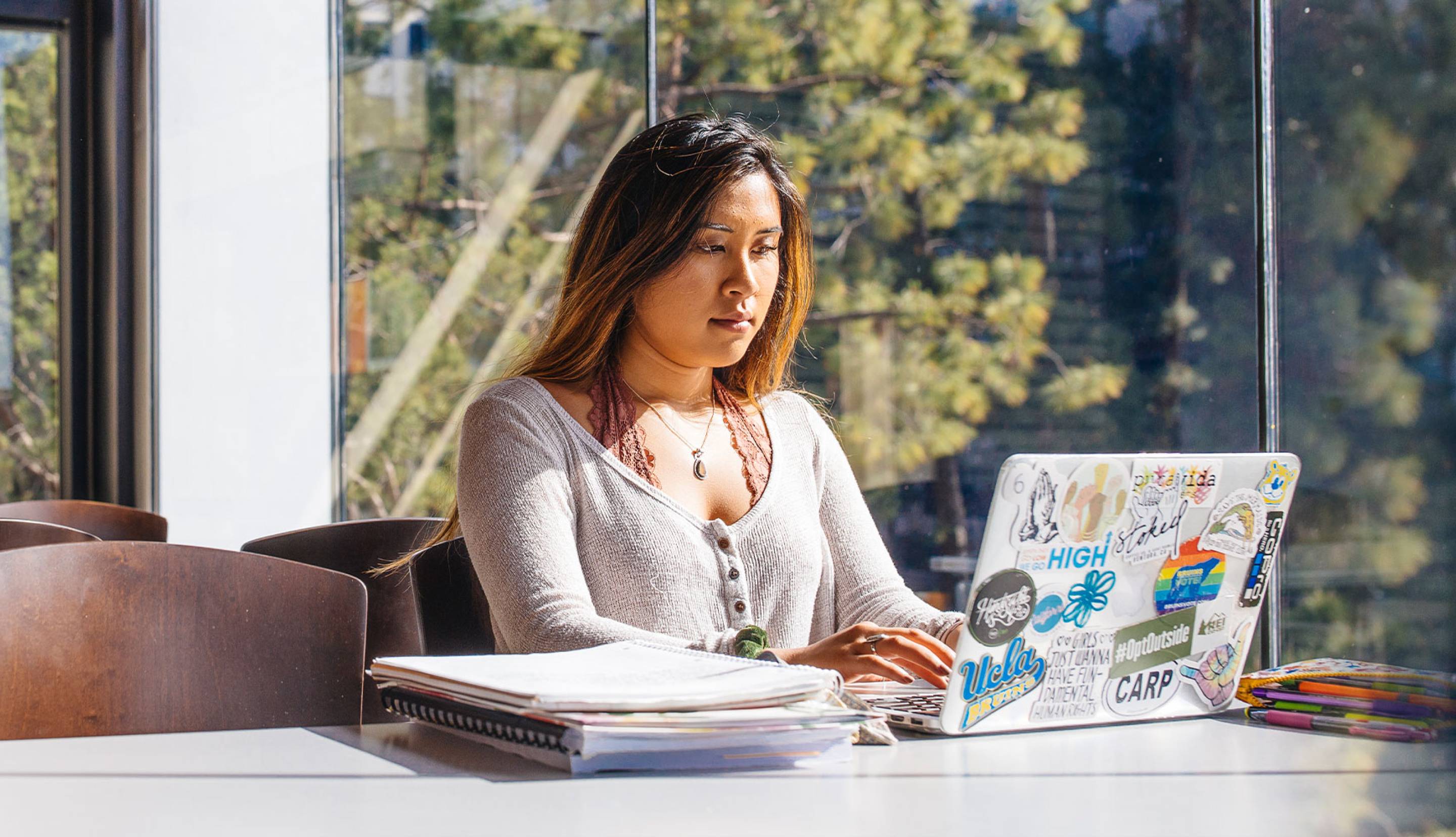 Woman on a computer working in front of a large glass window. 