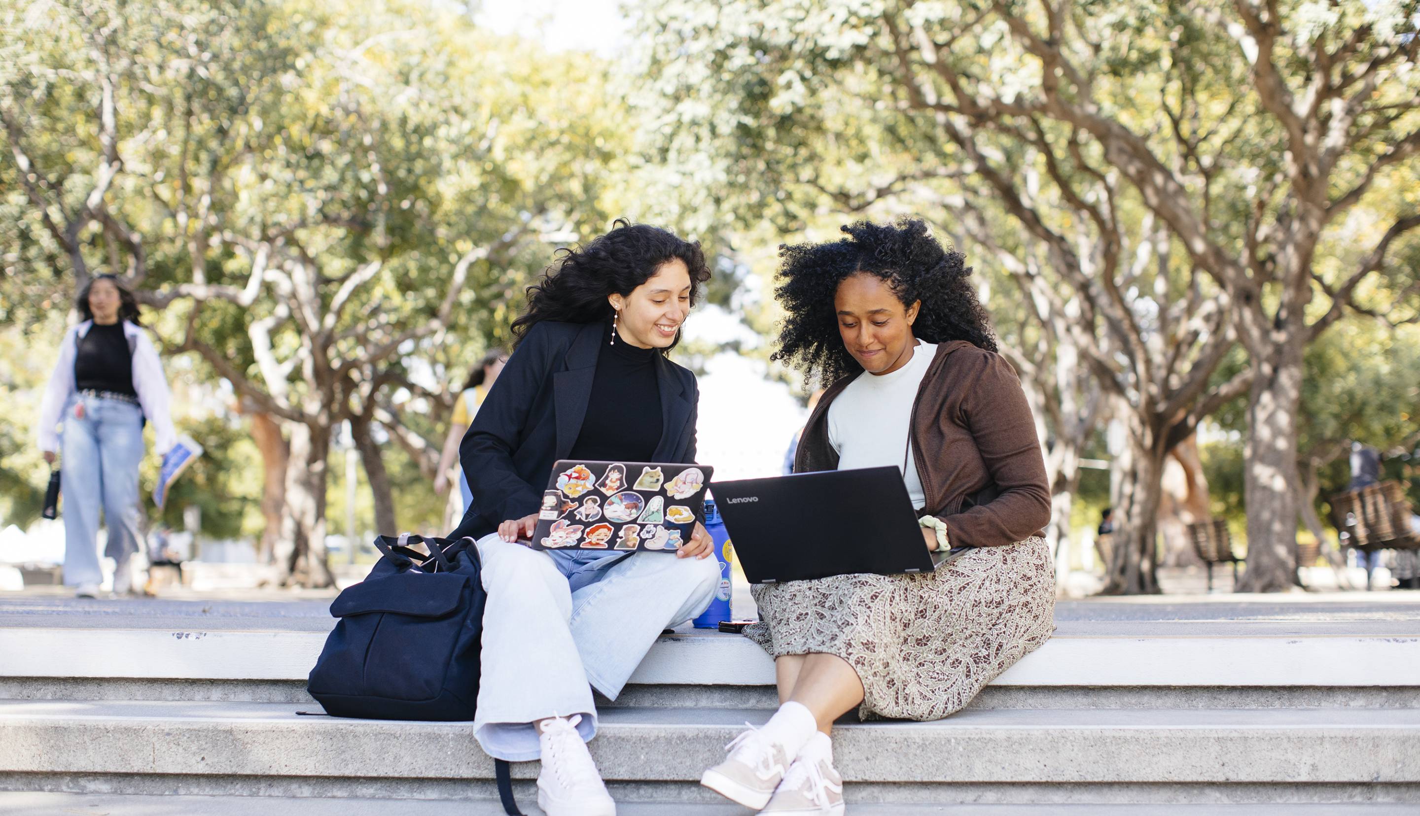 Two students sit on steps together on UC Irvine campus looking at their laptops