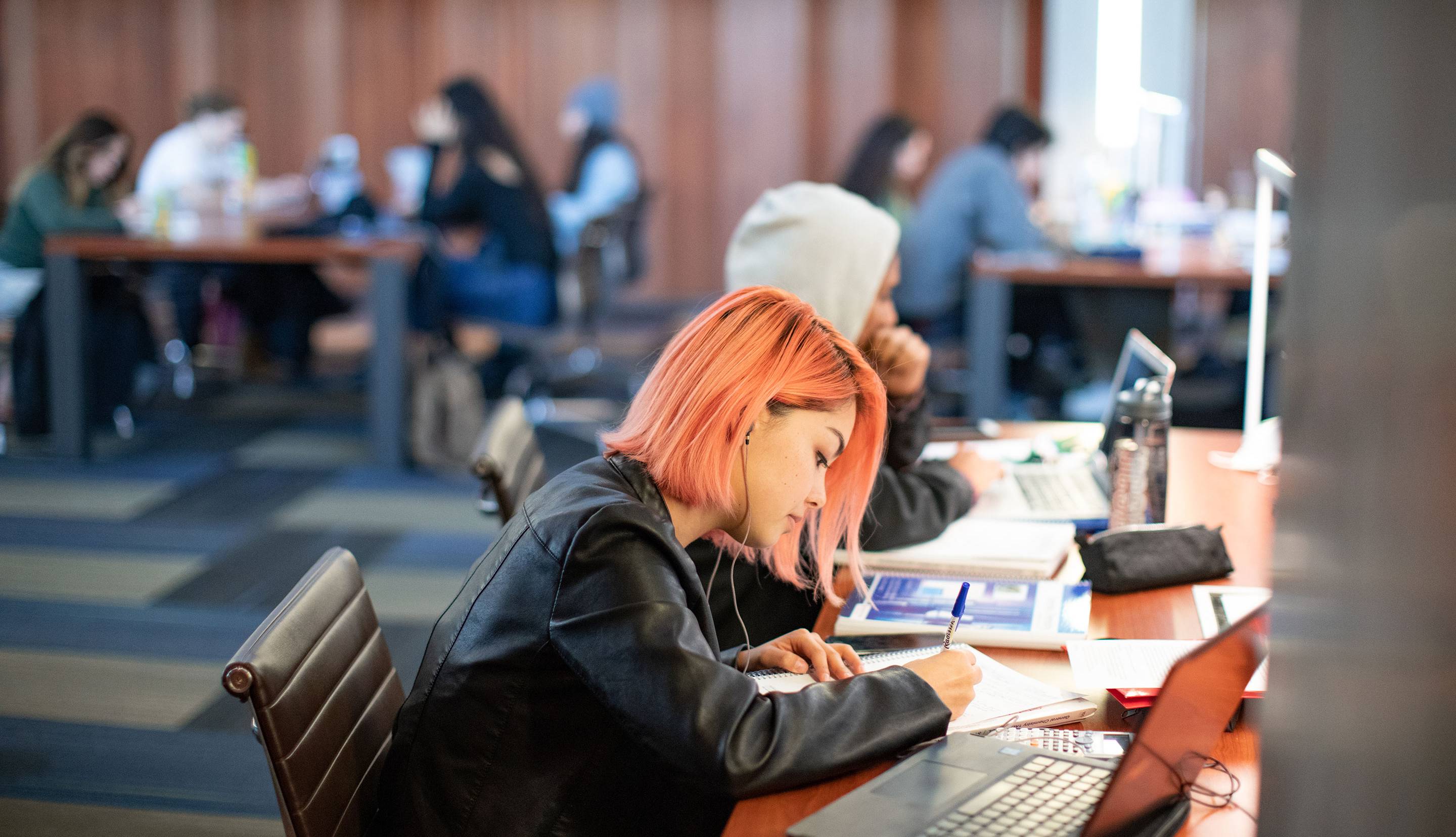 Student with pink hair sitting at a desk writing. 