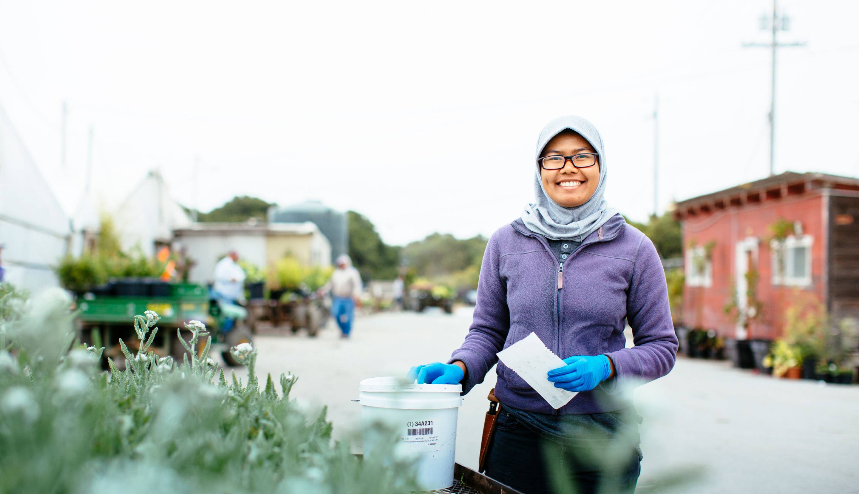 Woman standing outside next to a row of green plants.