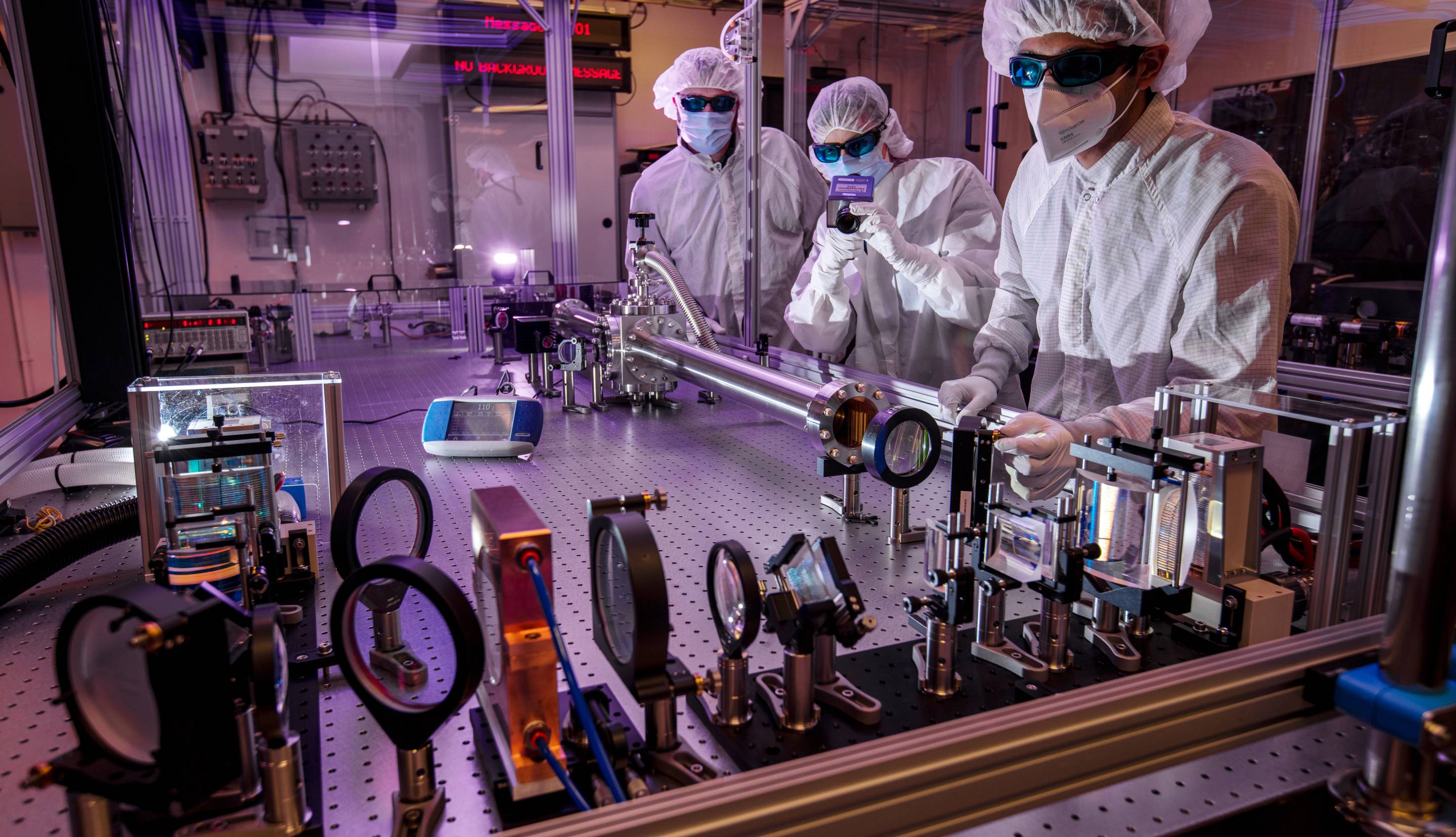 Three scientists in PPE and hazmat suits work in a lab