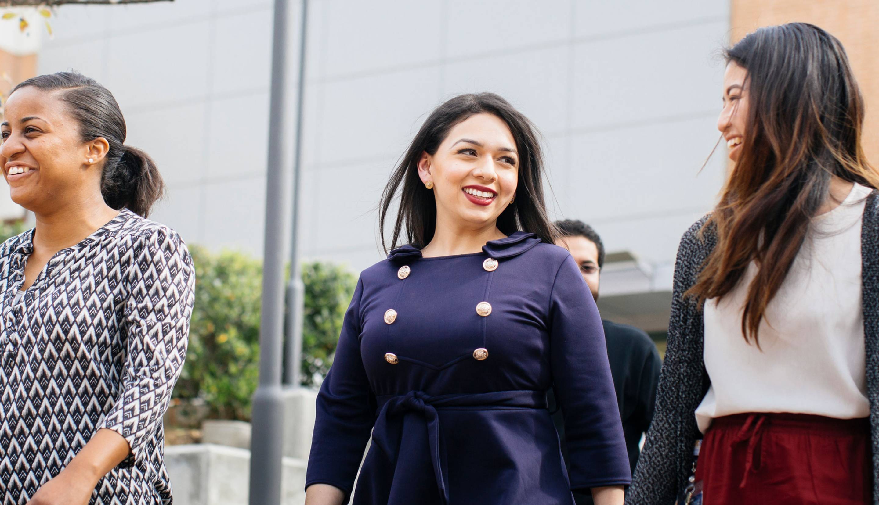 Three women walking and smiling outdoors, dressed in business attire 