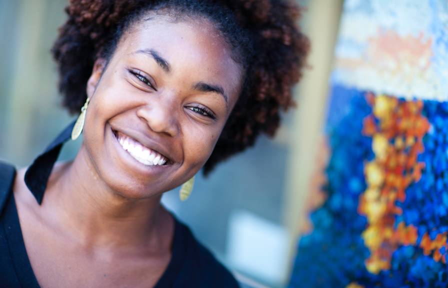 Young Black woman smiling looks at camera, colorful image behind her in background