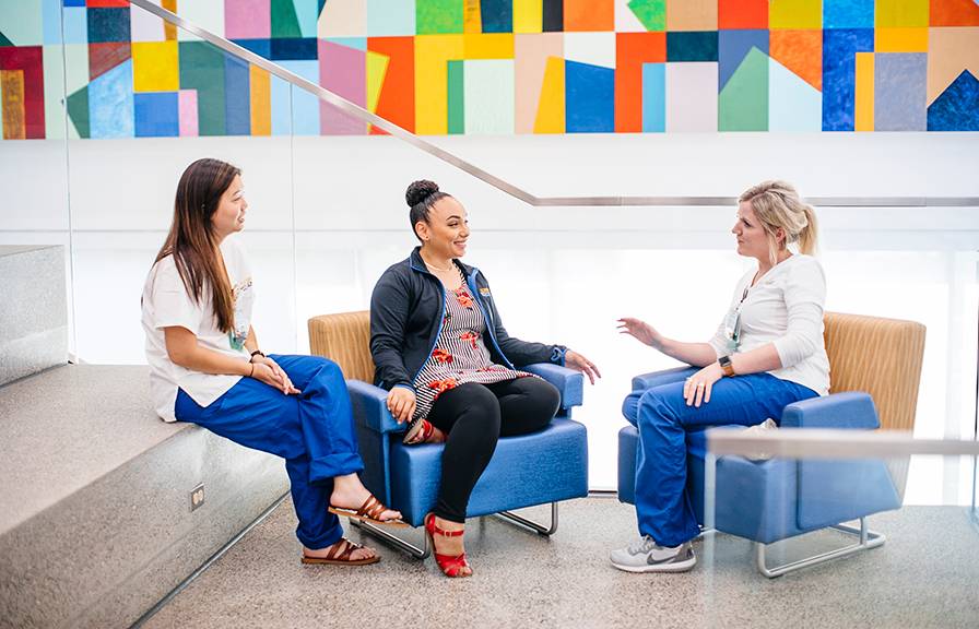 Three women talk together in a colorful seating area
