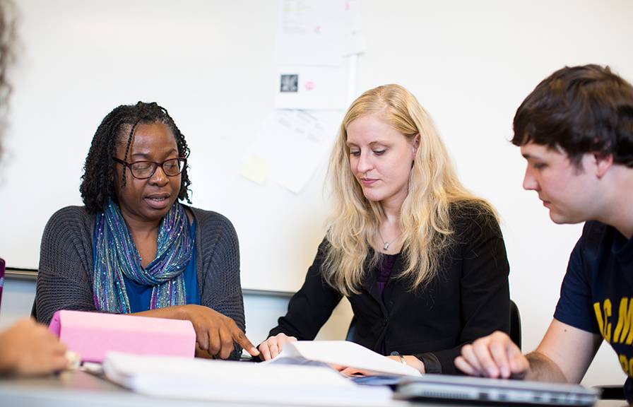 A Black woman a white woman and a young white man look at a piece of paper together