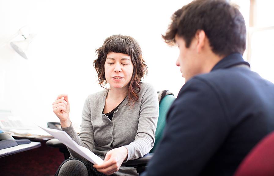 A white woman with mid-length hair shows a young man something in a binder