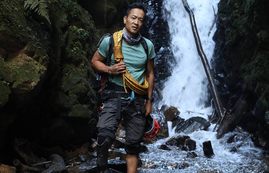 National geographic explorer with climbing gear in front of waterfall