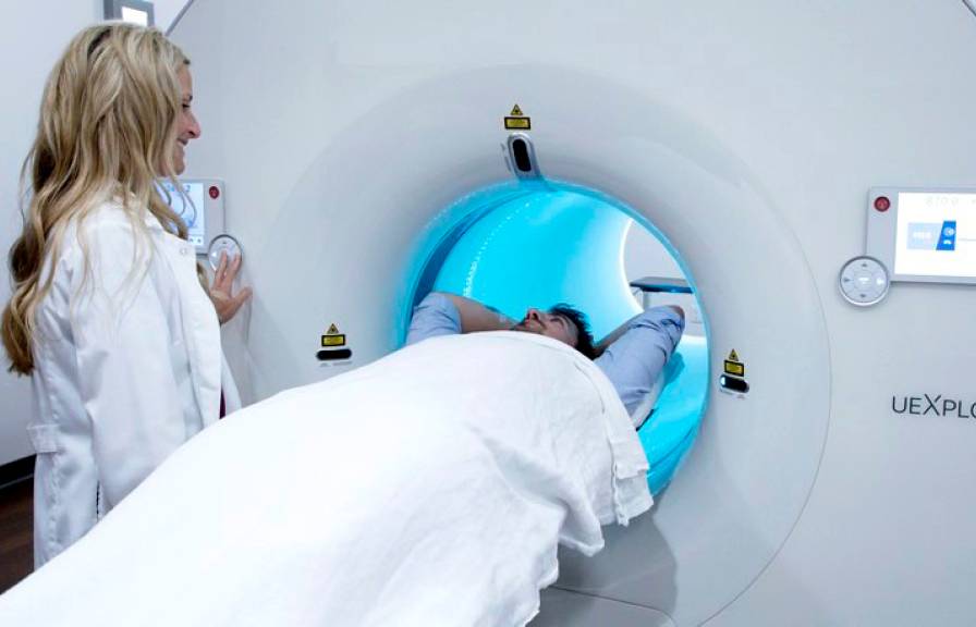 A technician standing by the side of a patient on the bed of the EXPLORER PET scanner