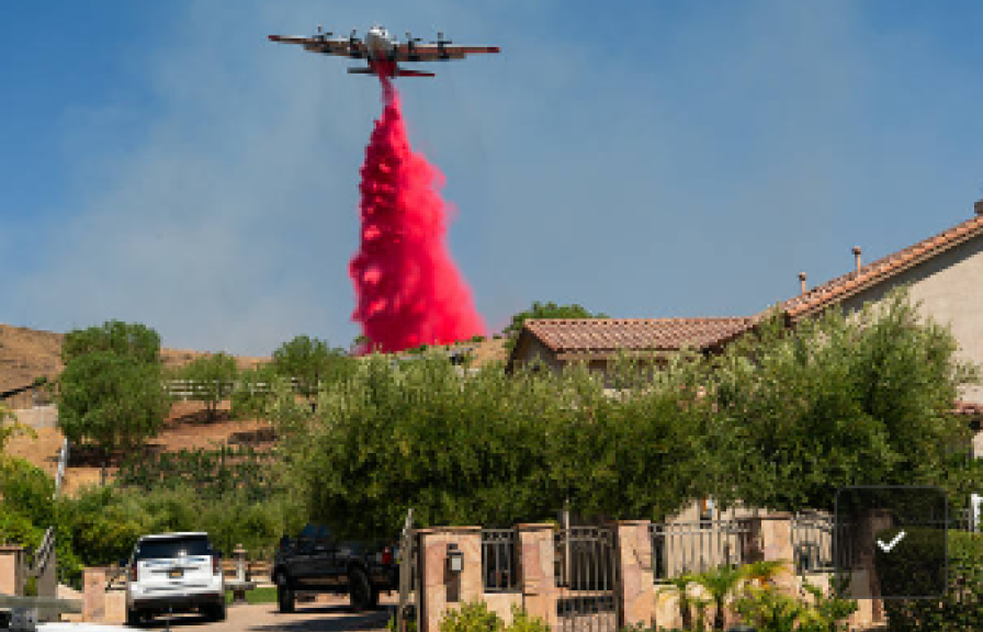 A plane dropping bright pink fire retardant with a suburban neighborhood in the foreground