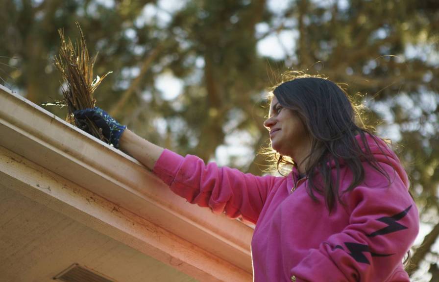 A woman cleaning plant debris out of a roof gutter