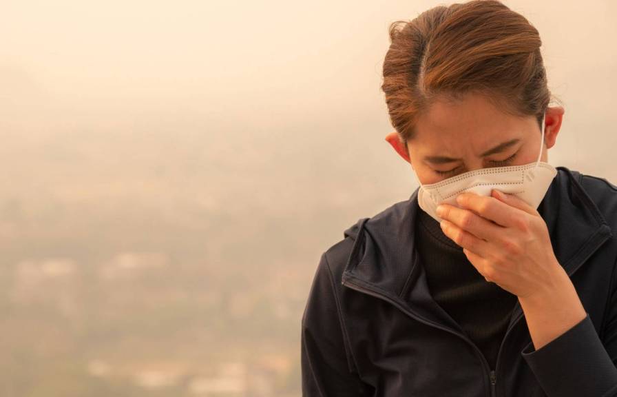 A woman wearing a mask struggling to breathe under smoke-filled sky