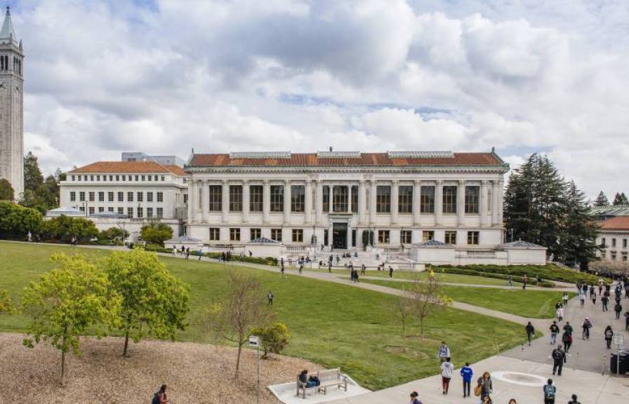 View of UC Berkeley's campus with a building, tower, and students crossing a large lawn.