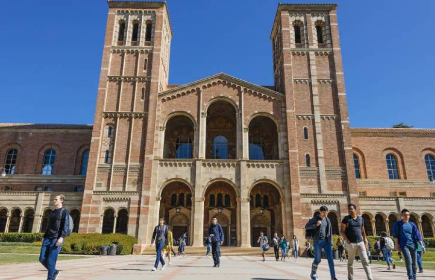 Students walk across the plaza in front of large brick building on the UCLA campus.