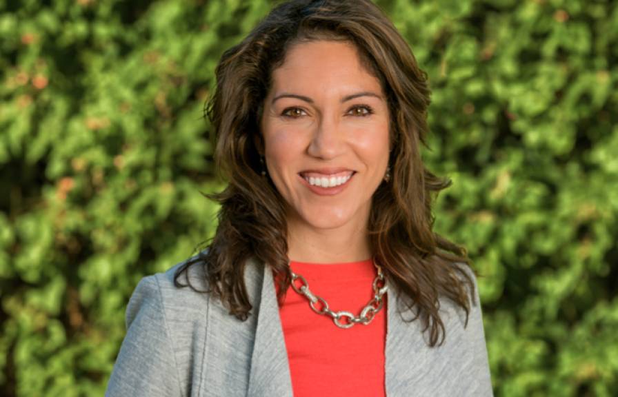 A woman in a gray blazer and red blouse smiles