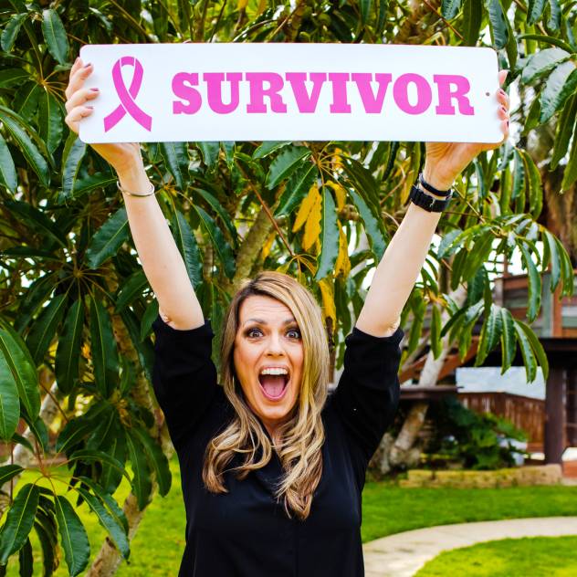 A woman looking very happy and holding a "survivor" sign with a pink breast cancer ribbon