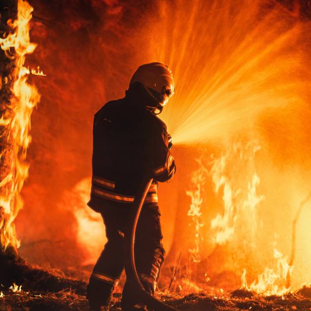 A firefighter using a hose to spray water on a wildfire burning through trees