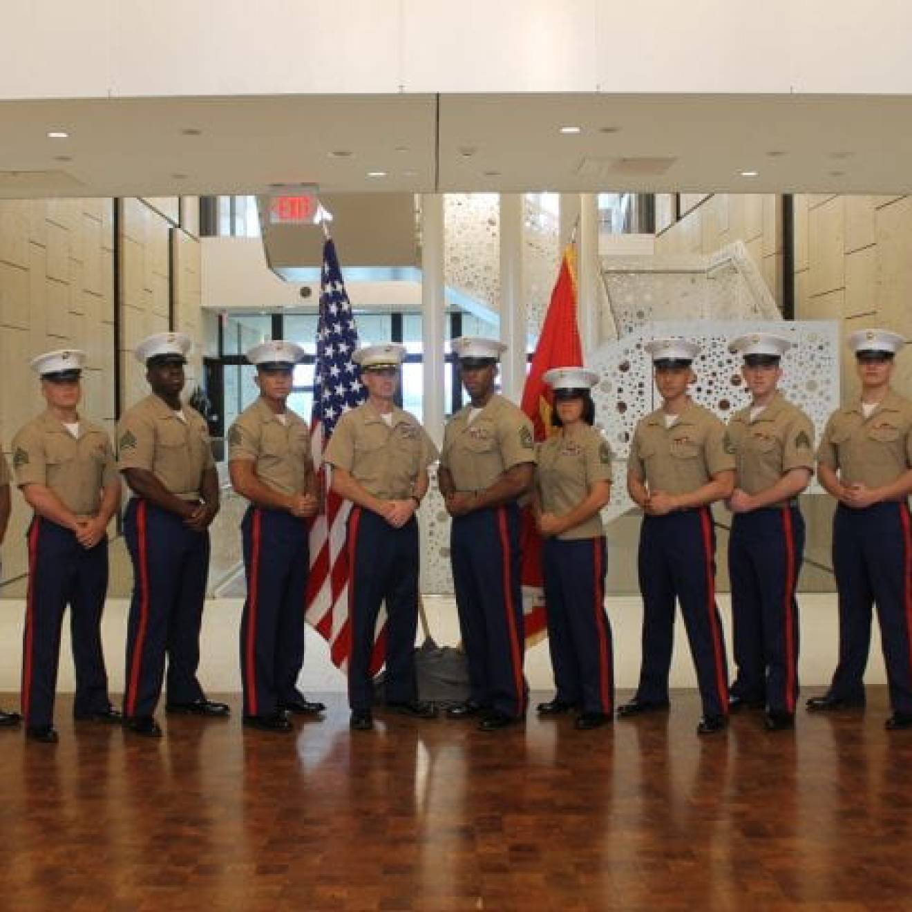 United States Marine Corps veteran and UCI sociology alumnus Andrew Truong ’23 (fourth from right), pictured with fellow service members, posing at ease in their uniforms in front of flags.