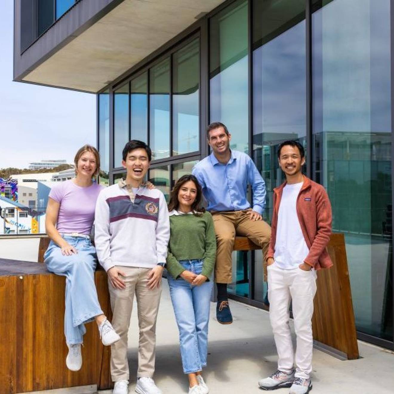 Five young people smile for the camera on an outdoor patio of an academic building