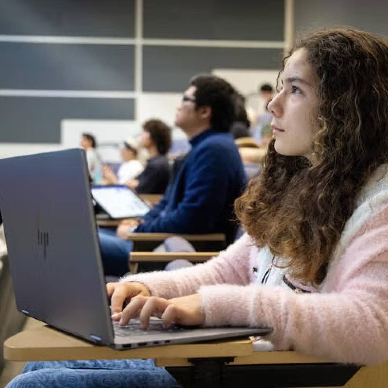 A pre-teen with long hair sits listening in a lecture hall