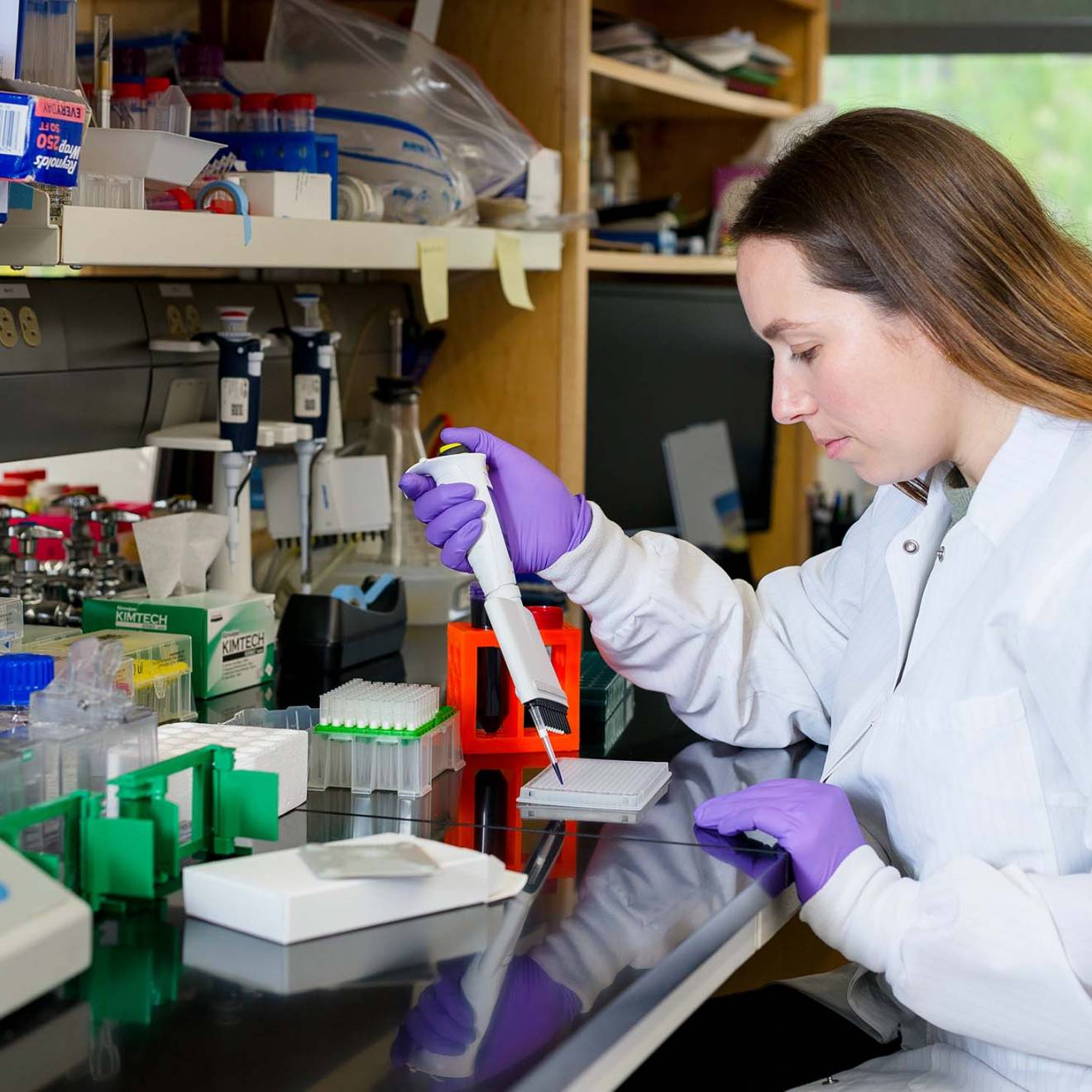 A student in a white lab coat with a pipette in the lab