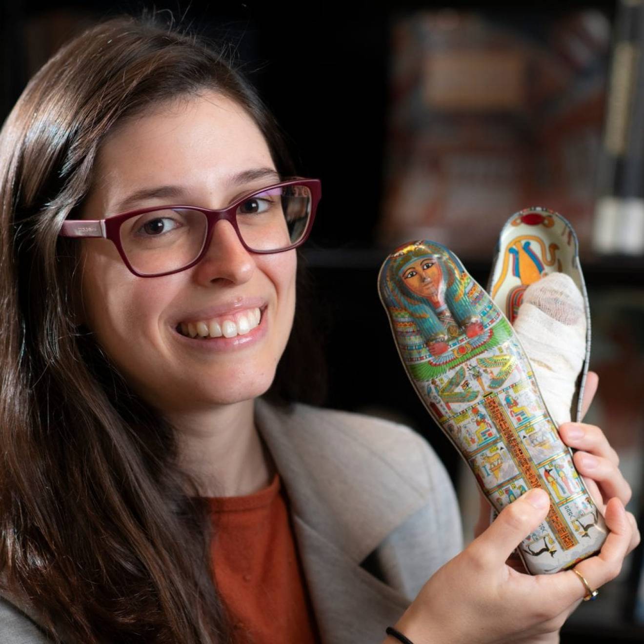 A person smiling and holding a small tin Egyptian coffin