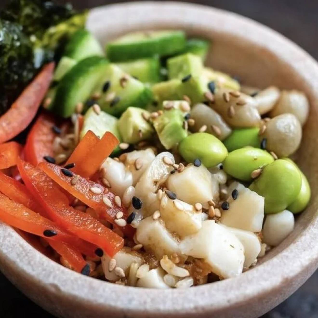 A poke bowl with vegetables, edamame, fish, sesame seeds and seaweed