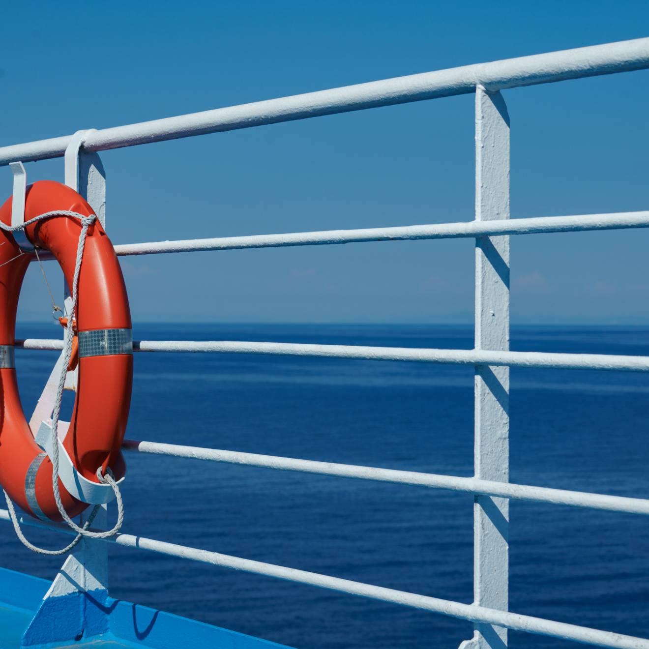 a red lifebuoy hangs on board a ferry cruise ship against the backdrop of a blue sea and a cloudless sky