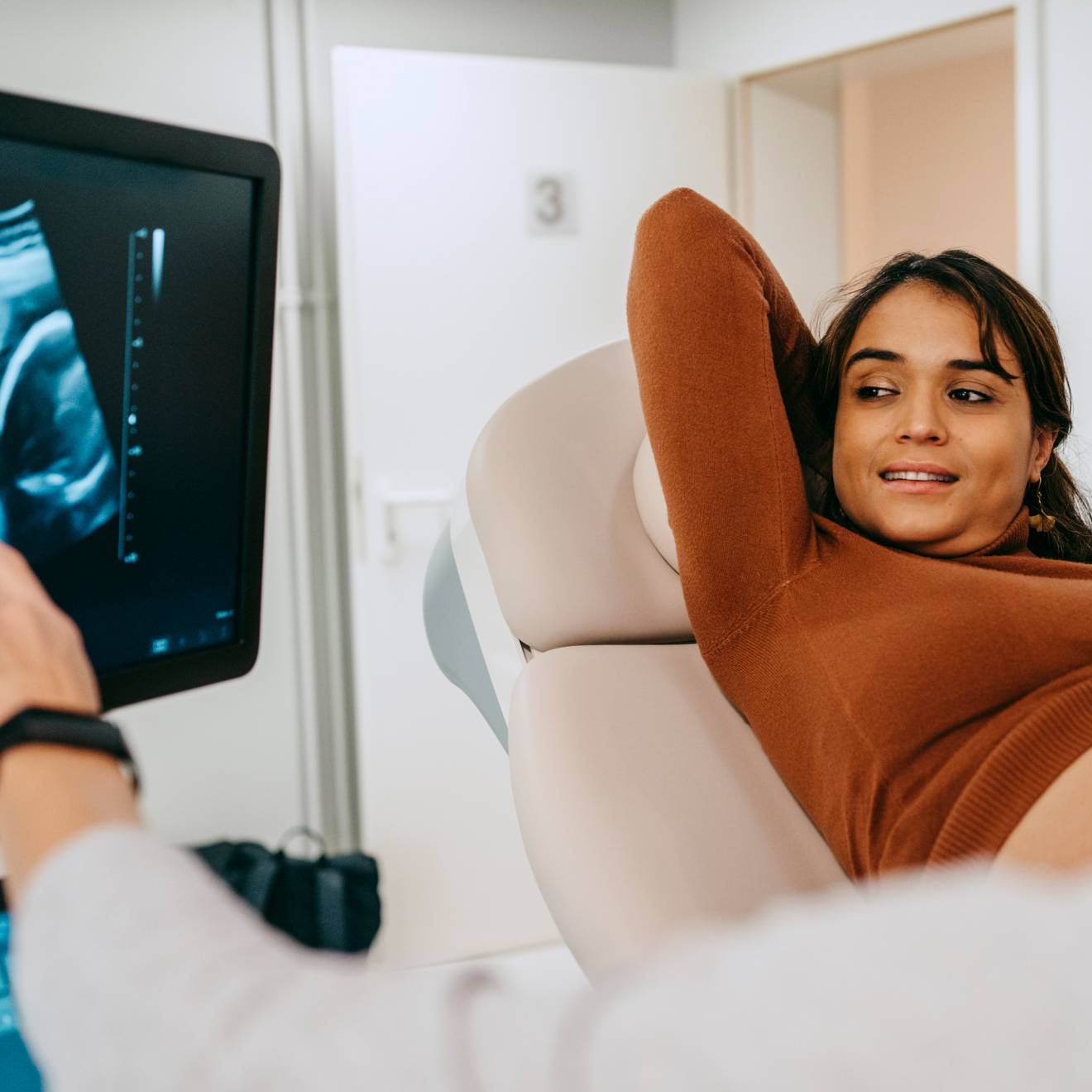 A woman looks happily at an image of her fetus on a screen as a nurse points