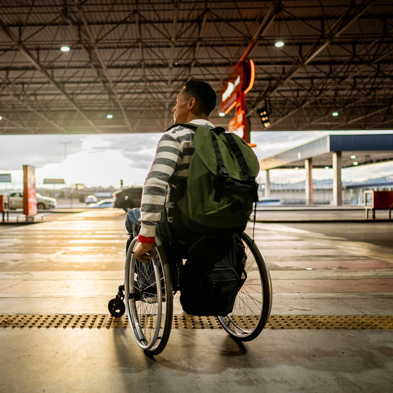 A person in a wheelchair with a backpack on is about to cross a roadway at a crosswalk