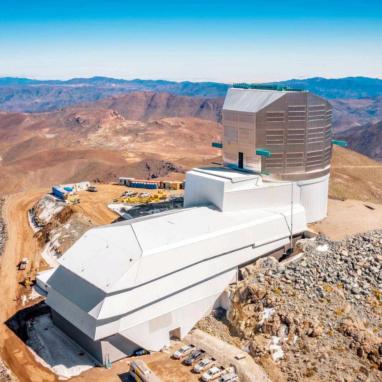 A huge, modern building atop a remote, snow-covered mountain, with desolate mountains stretching into the distance