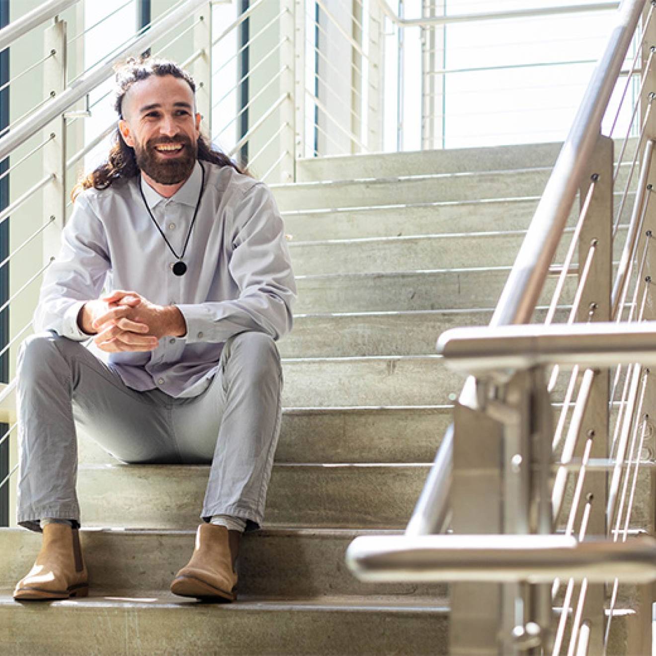 Trevor Auldridge-Reveles sits in a concrete and steel staircase, leaning elbows on legs, smiling