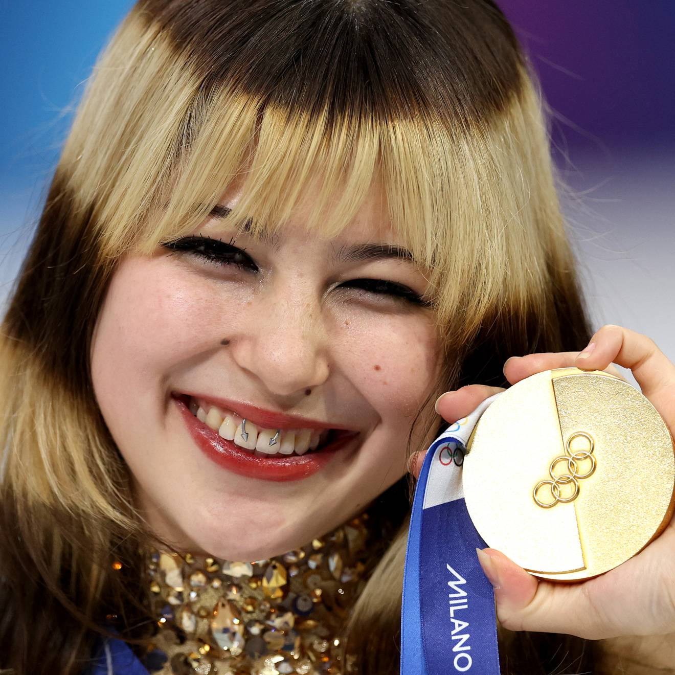 A woman holds up a gold medal and smiles