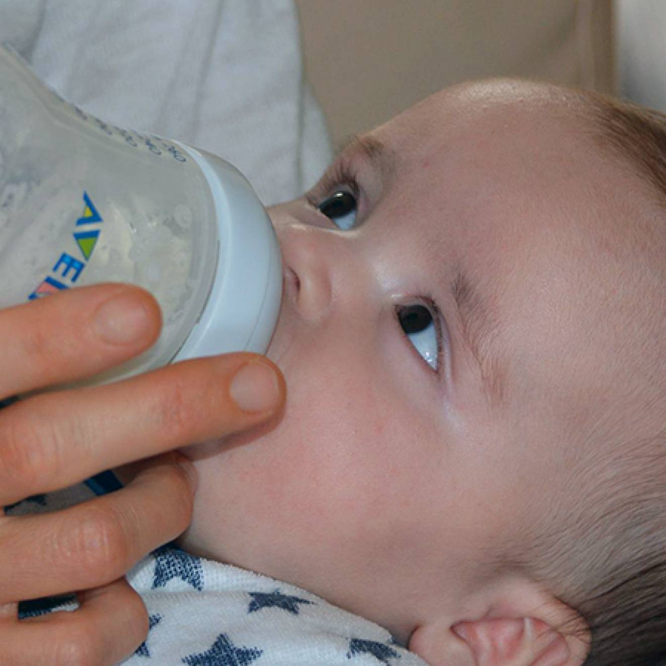 Baby drinking from a bottle looking up at person feeding