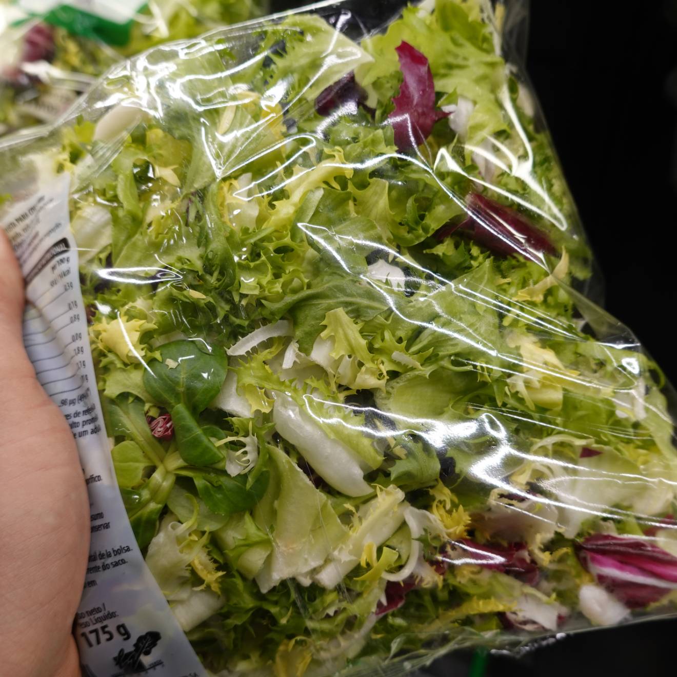 A hand holds a bag of salad greens at a grocery store