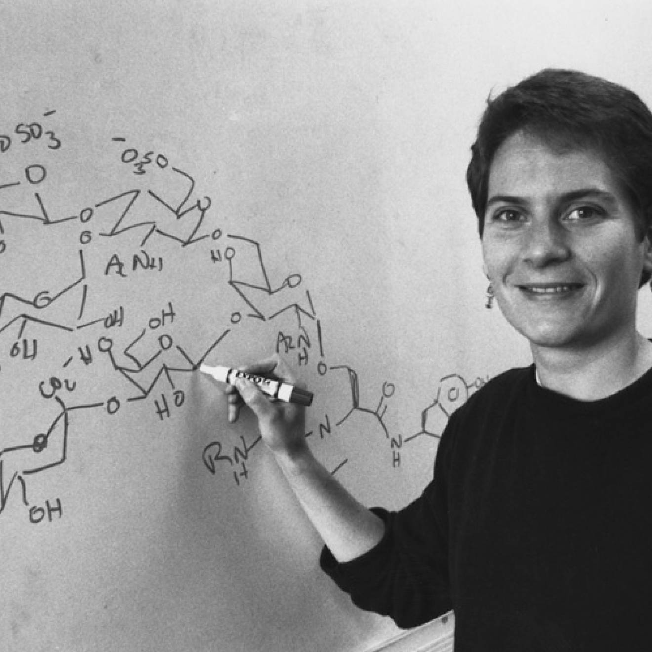 Black and white photo of Carolyn Bertozzi at a chalkboard