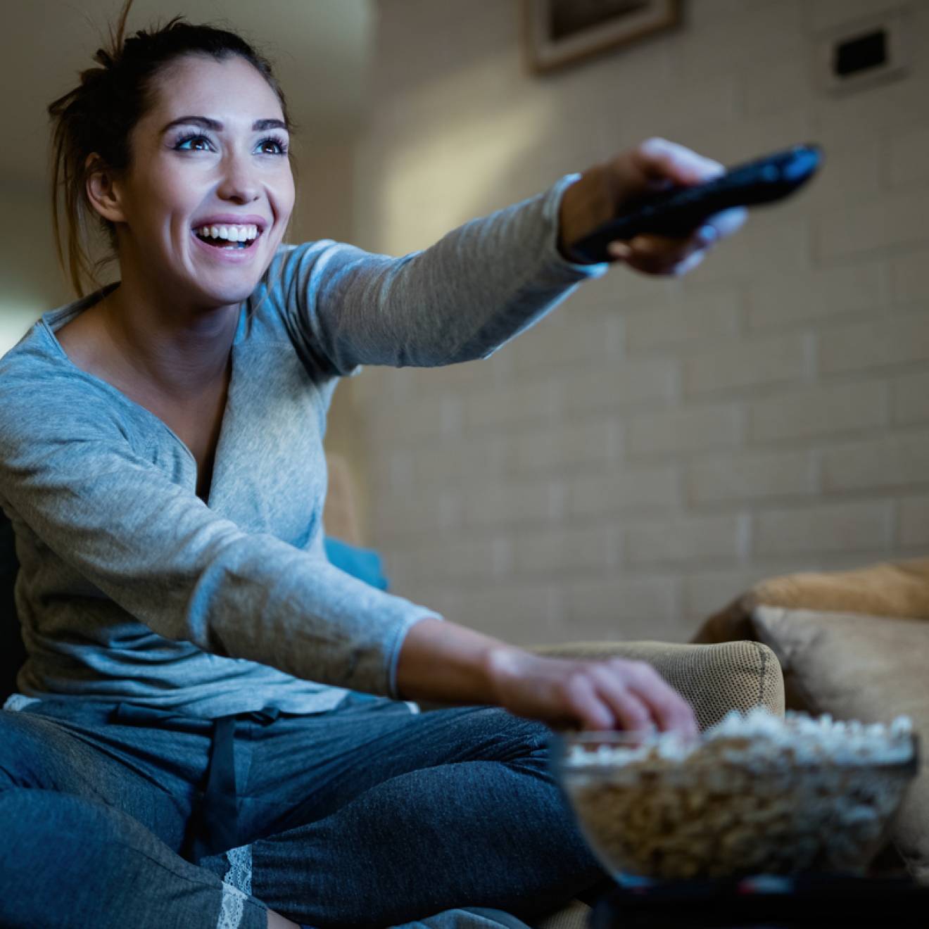 A young woman smiling holding a remote and eating popcorn