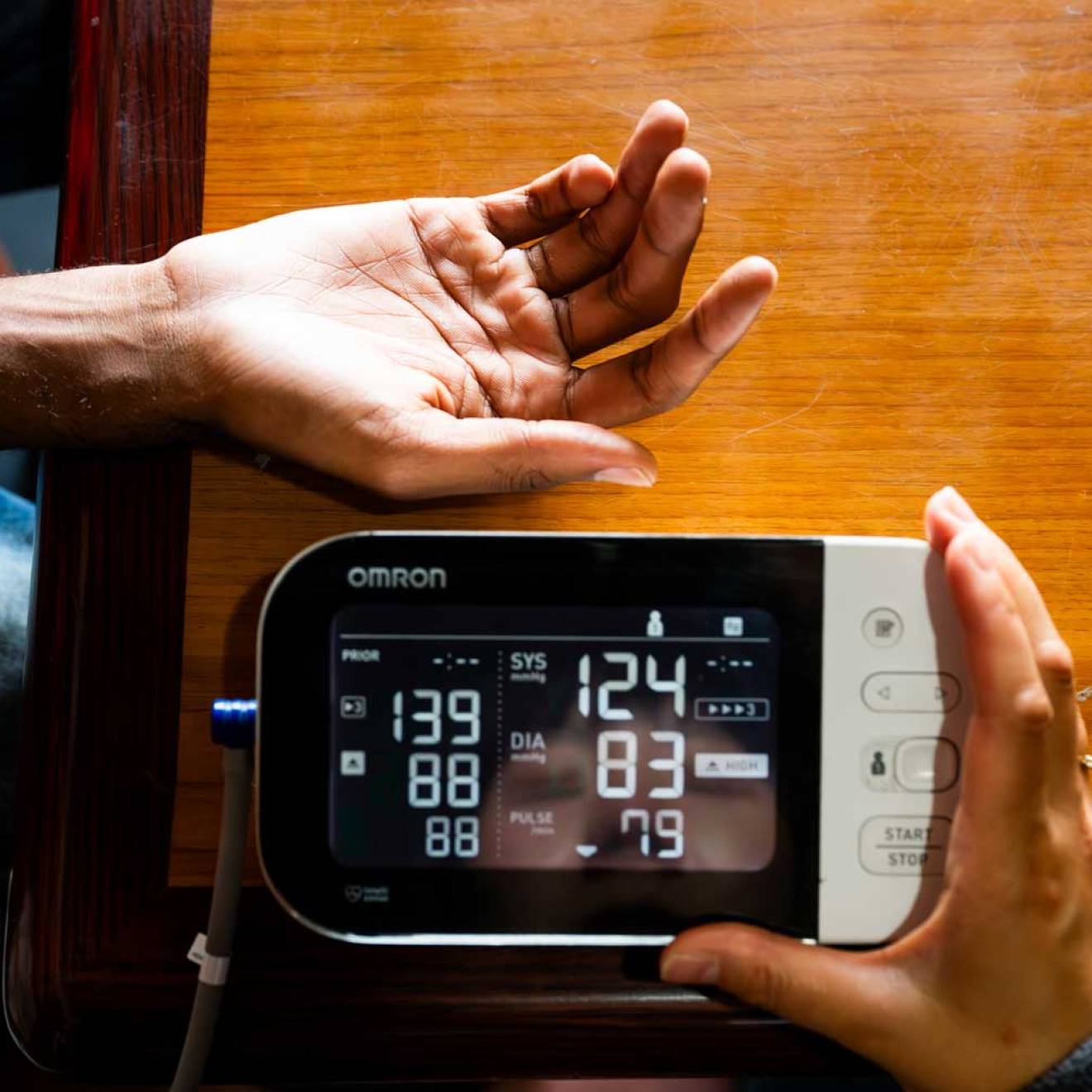 A hand is extended while another hand holds a blood pressure monitor with readings on it