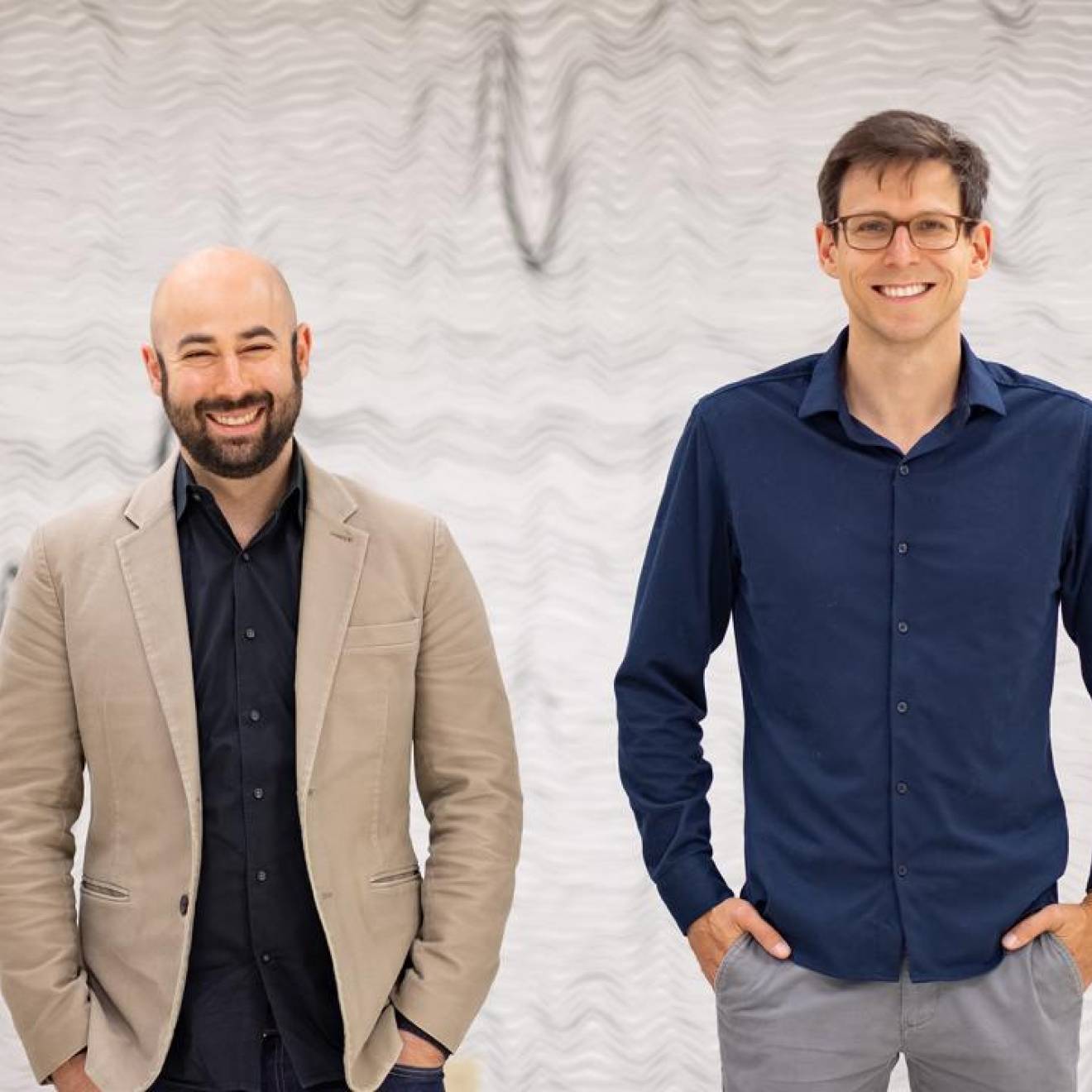 Two men standing together in front of a backdrop of wavy lines