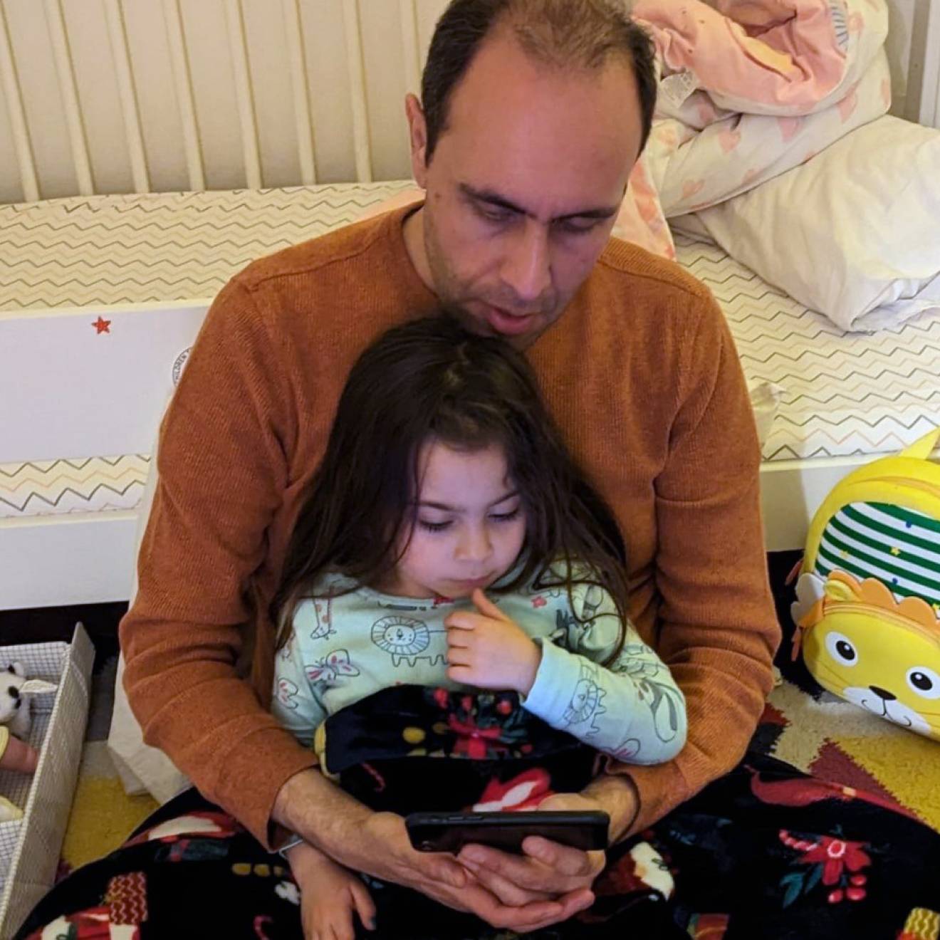 A balding man holds a young daughter as they read together, looking at a screen
