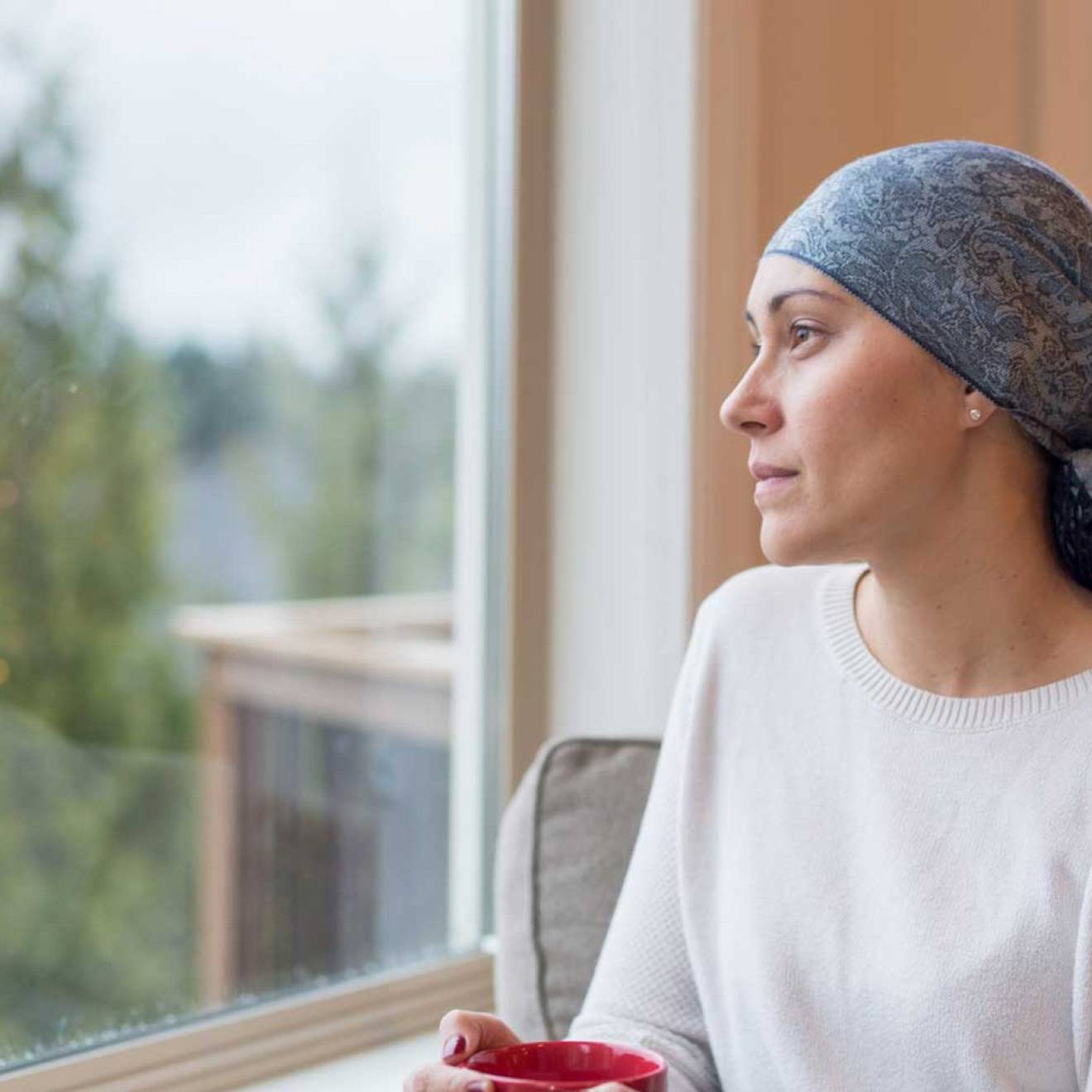 Woman recovering from breast cancer wearing a scarf on her head stares out the window